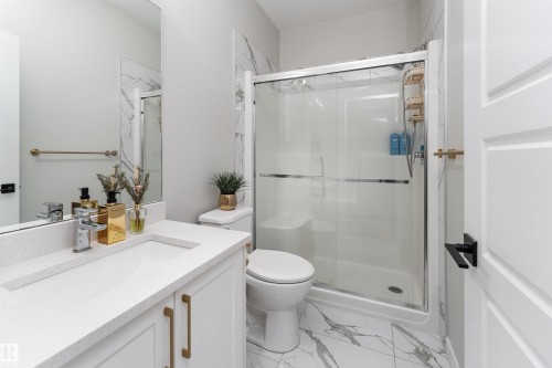 The bathroom features a modern vanity with a white countertop and gold-toned hardware, a spacious shower with a clear glass enclosure, and white marble-patterned floor tiles - 993 Berg Pl, Leduc, AB - Indoor Photo Showing Bathroom