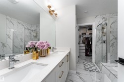A bathroom featuring a dual vanity with white countertops, gold-toned hardware, and a large mirror - 