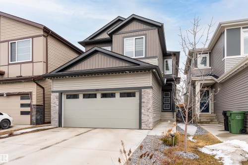 The property features a two-car garage, a paved driveway, and stone accent siding - 993 Berg Pl, Leduc, AB - Outdoor With Facade