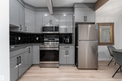 Modern kitchen featuring light grey cabinetry with black hardware, stainless steel appliances, and a black marble-style backsplash - 