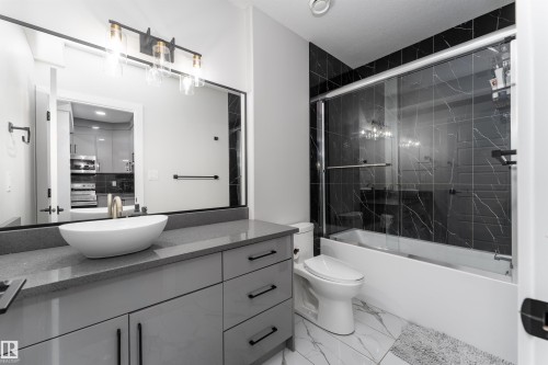 The bathroom features a modern vanity with a vessel sink, a large mirror, and a shower-tub combination with black marble-style tiling and a glass enclosure - 993 Berg Pl, Leduc, AB - Indoor Photo Showing Bathroom