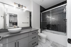 The bathroom features a modern vanity with a vessel sink, a large mirror, and a shower-tub combination with black marble-style tiling and a glass enclosure - 