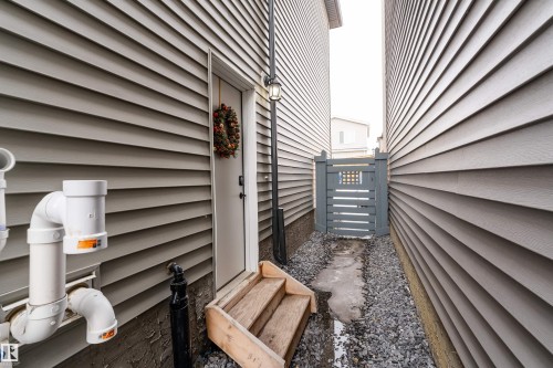 The property features gray siding, a white exterior door with wooden steps, and a gray gate in a gravel path - 993 Berg Pl, Leduc, AB - Outdoor