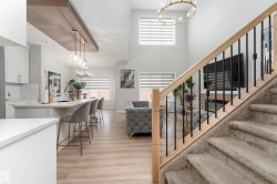 The property features an open-concept layout with light wood-style flooring, a kitchen island with seating, and a carpeted staircase with a light wood handrail and black balusters - 