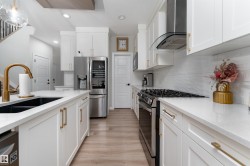 The kitchen features white cabinetry with gold-toned hardware, white countertops, and stainless steel appliances including a refrigerator and range with a hood - 