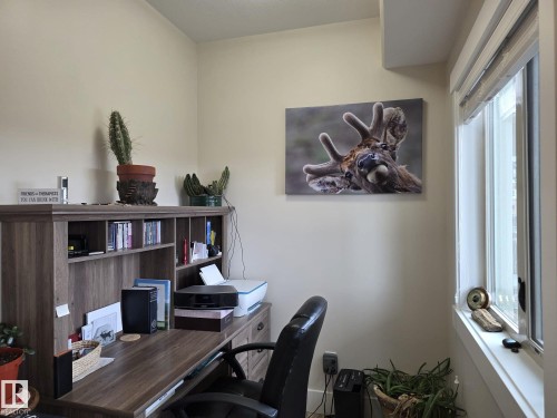 This room features a window providing natural light, warm neutral wall tones, and a wood-toned desk with integrated shelving - 304 5201 Brougham Drive, Drayton Valley, AB - Indoor Photo Showing Office