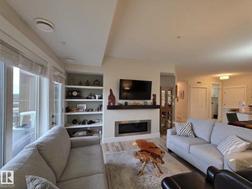 The living room features a contemporary linear fireplace, built-in shelving, and a glass door leading to an outdoor space - 304 5201 Brougham Drive, Drayton Valley, AB - Indoor Photo Showing Living Room With Fireplace