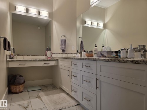 The bathroom features a dual vanity with light-colored cabinetry, a granite countertop, and integrated sinks with modern faucets - 304 5201 Brougham Drive, Drayton Valley, AB - Indoor