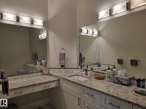 Bathroom featuring granite countertops, extensive mirror space, white cabinetry, and modern light fixtures - 304 5201 Brougham Drive, Drayton Valley, AB - Indoor Photo Showing Bathroom