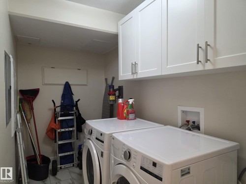 Laundry area featuring white cabinetry with brushed nickel hardware, light-colored walls, and a tiled floor - 304 5201 Brougham Drive, Drayton Valley, AB - Indoor Photo Showing Laundry Room