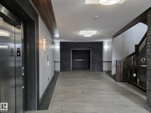 The property features a contemporary entryway with light-colored tile flooring, accent walls with dark stacked stone, and a dark wood staircase with a matching console table - 304 5201 Brougham Drive, Drayton Valley, AB - Indoor Photo Showing Other Room