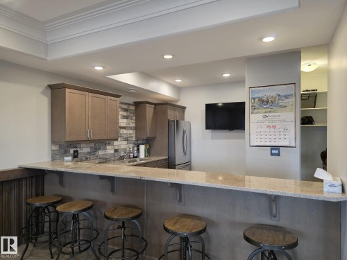 The property features a well-appointed wet bar with a light-colored countertop, recessed lighting, and a backsplash with varied stone-look tiles - 304 5201 Brougham Drive, Drayton Valley, AB - Indoor Photo Showing Kitchen With Upgraded Kitchen
