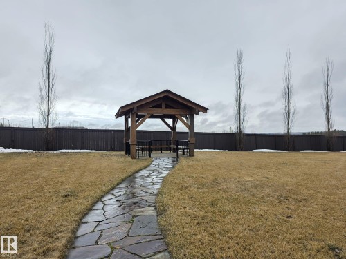 The property features a spacious yard with a natural stone pathway leading to a wooden gazebo, complete with seating - 304 5201 Brougham Drive, Drayton Valley, AB - Outdoor