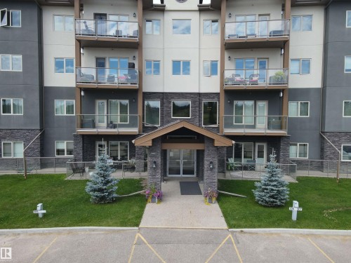 The property features a multi-story building with a facade of light and dark grey siding, accented with stone detailing - 304 5201 Brougham Drive, Drayton Valley, AB - Outdoor With Balcony With Facade