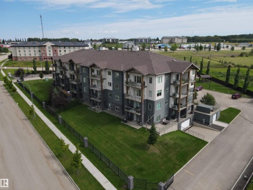 The property features a multi-story building with a dark shingled roof, a paved road with a sidewalk, and a well-maintained lawn area - 304 5201 Brougham Drive, Drayton Valley, AB - Outdoor With View