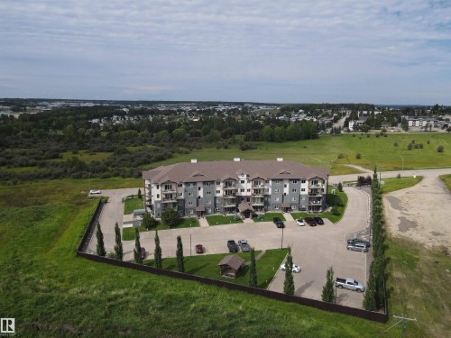 The property features a multi-story building with a brown roof and grey siding, surrounded by extensive green spaces - 304 5201 Brougham Drive, Drayton Valley, AB - Outdoor With View