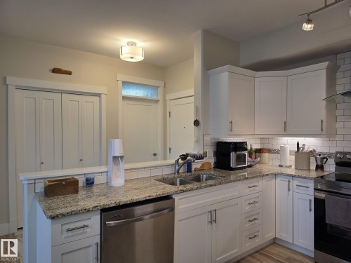 The kitchen features white cabinetry, granite countertops, a stainless steel dishwasher, and a subway tile backsplash - 304 5201 Brougham Drive, Drayton Valley, AB - Indoor Photo Showing Kitchen With Double Sink