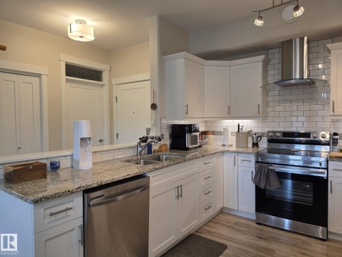 The kitchen features white cabinetry, granite countertops, a subway tile backsplash, and stainless steel appliances including a range and dishwasher - 304 5201 Brougham Drive, Drayton Valley, AB - Indoor Photo Showing Kitchen With Double Sink