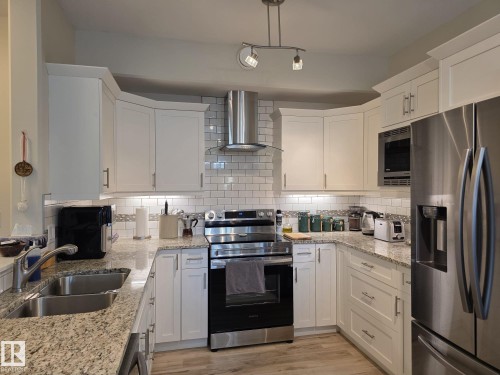 The kitchen features white cabinetry, granite countertops, a stainless steel refrigerator, and a subway tile backsplash - 304 5201 Brougham Drive, Drayton Valley, AB - Indoor Photo Showing Kitchen With Double Sink With Upgraded Kitchen