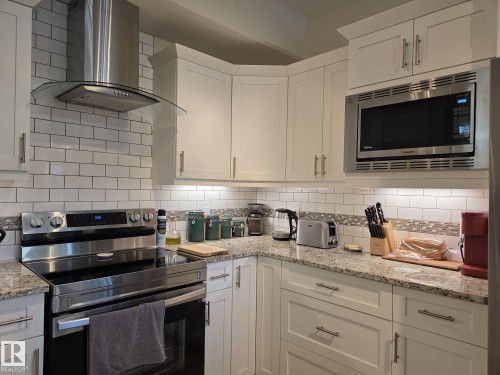 The kitchen features white cabinetry, stainless steel appliances, granite countertops, and a subway tile backsplash with decorative accents - 304 5201 Brougham Drive, Drayton Valley, AB - Indoor Photo Showing Kitchen With Upgraded Kitchen