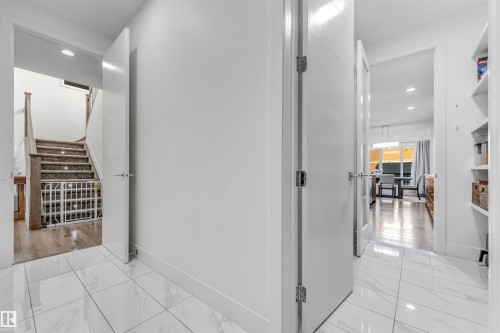 The property features white tile flooring and white walls throughout the hallway, with a staircase visible in the background and an additional room with wood flooring visible through an open doorway - 1407 Graydon Hill Way, Edmonton, AB - Indoor Photo Showing Other Room