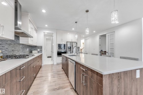 Modern kitchen featuring white upper cabinets, wood-look lower cabinets, stainless steel appliances, and a large island with a white countertop - 1407 Graydon Hill Way, Edmonton, AB - Indoor Photo Showing Kitchen With Upgraded Kitchen