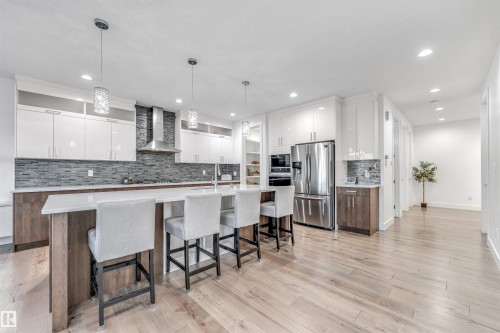 The kitchen features an island with seating, a stainless steel refrigerator, white cabinetry, and light wood flooring - 1407 Graydon Hill Way, Edmonton, AB - Indoor Photo Showing Kitchen With Upgraded Kitchen