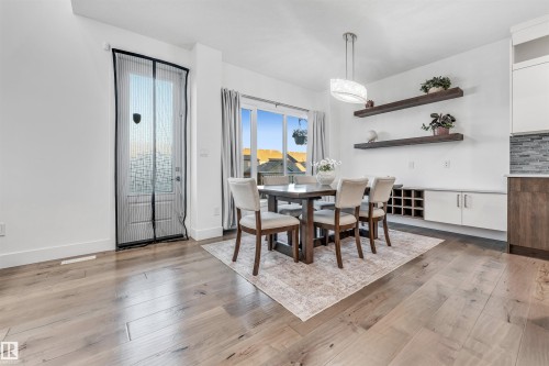 This dining area features light-toned hardwood flooring, a modern chandelier, and a built-in credenza with wine storage - 1407 Graydon Hill Way, Edmonton, AB - Indoor Photo Showing Dining Room