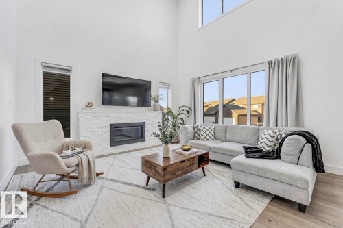 The living room features vaulted ceilings, large windows providing natural light, and a fireplace with a stone surround - 1407 Graydon Hill Way, Edmonton, AB - Indoor Photo Showing Living Room With Fireplace