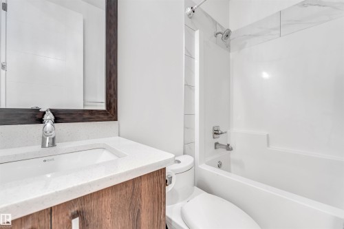 Bathroom featuring a vanity with a white countertop and a dark wood-framed mirror, a white toilet, and a bathtub with a shower - 1407 Graydon Hill Way, Edmonton, AB - Indoor Photo Showing Bathroom
