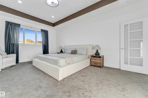 This spacious room features light gray carpeting, a large window with blue curtains, and a white door with frosted glass panels - 1407 Graydon Hill Way, Edmonton, AB - Indoor Photo Showing Bedroom