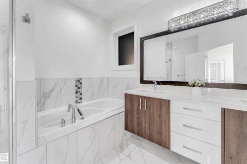 The bathroom features a spacious bathtub with a tiled surround, a large vanity with a white countertop, and a wide mirror illuminated by an overhead light fixture - 1407 Graydon Hill Way, Edmonton, AB - Indoor Photo Showing Bathroom