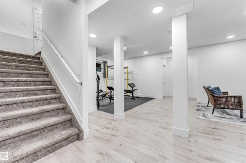 This property features a spacious area with light-toned flooring, recessed lighting, and a white handrail along the carpeted stairs - 1407 Graydon Hill Way, Edmonton, AB - Indoor Photo Showing Other Room