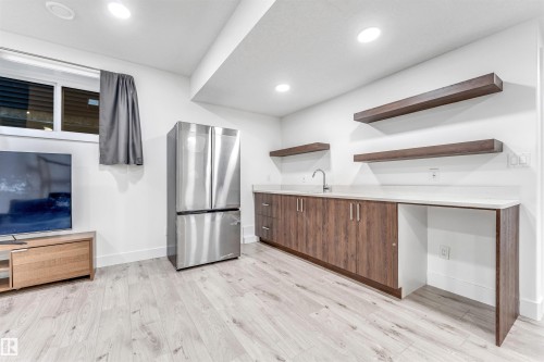 This versatile space features light-toned flooring, a stainless steel refrigerator, and a built-in counter with a sink and dark wood cabinetry - 1407 Graydon Hill Way, Edmonton, AB - Indoor Photo Showing Kitchen