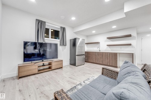 Recreation room featuring light wood flooring, recessed lighting, and a wet bar with a stainless steel refrigerator, sink, and wood cabinetry - 1407 Graydon Hill Way, Edmonton, AB - Indoor