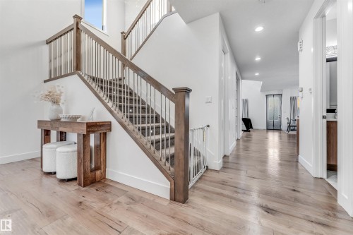 Elegant staircase with dark wood banister and light-colored balusters, complemented by light hardwood flooring throughout the hall - 1407 Graydon Hill Way, Edmonton, AB - Indoor Photo Showing Other Room