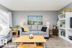 Living room featuring light grey walls, light-colored flooring, and a large window with white curtains - 