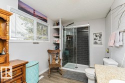 This bathroom features a shower with dark subway tile, a window providing natural light, and a vanity with a light-colored countertop - 
