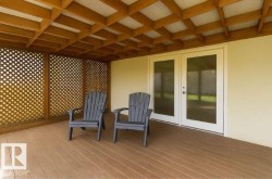 Covered deck area featuring a patterned wooden ceiling, wooden lattice privacy screens, and a pair of white double doors with glass panels - 