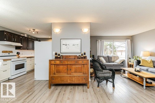 Bright interior space featuring light-toned flooring, a kitchen with dark upper cabinetry and light lower cabinetry, and a living area with a sliding glass door - 8 Duke Drive, Lamont, AB - Indoor