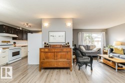 Bright interior space featuring light-toned flooring, a kitchen with dark upper cabinetry and light lower cabinetry, and a living area with a sliding glass door - 