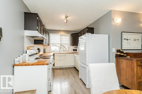 The kitchen features white appliances, dark upper cabinetry, white lower cabinetry, and light wood countertops - 8 Duke Drive, Lamont, AB - Indoor Photo Showing Kitchen