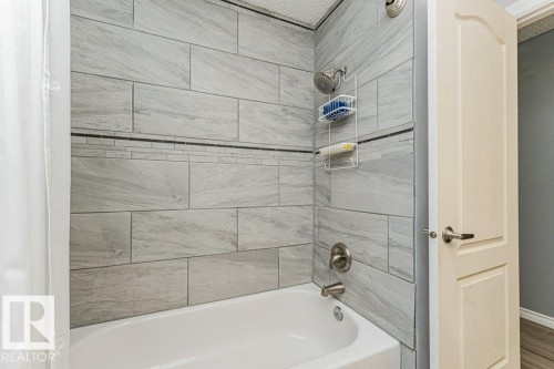 The bathroom features a bathtub with a tiled shower surround, including a decorative mosaic accent strip - 8 Duke Drive, Lamont, AB - Indoor Photo Showing Bathroom