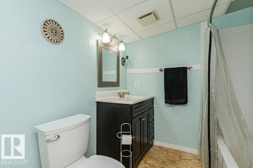 The bathroom features a toilet, a vanity with a mirror and overhead lighting, and a shower with a clear shower curtain - 8 Duke Drive, Lamont, AB - Indoor Photo Showing Bathroom