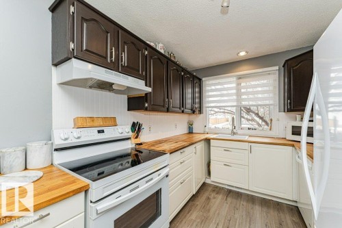 The kitchen features dark upper cabinetry, white lower cabinetry, and wood countertops, complemented by a white beadboard backsplash - 8 Duke Drive, Lamont, AB - Indoor Photo Showing Kitchen