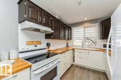The kitchen features dark upper cabinetry, white lower cabinetry, and wood countertops, complemented by a white beadboard backsplash - 