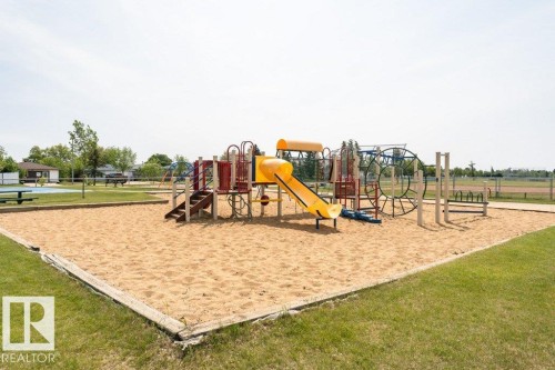 A community amenity featuring a sand area with a colorful playground structure, surrounded by a grassy lawn - 8 Duke Drive, Lamont, AB - Outdoor