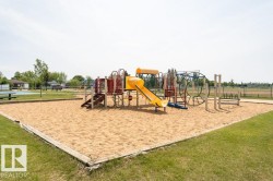 A community amenity featuring a sand area with a colorful playground structure, surrounded by a grassy lawn - 