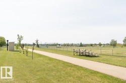 This community area features an extensive grassy field, a paved walking path, and bleachers, all surrounded by a chain-link fence - 