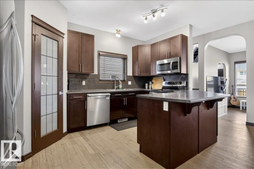 Kitchen featuring wood cabinetry, stainless steel appliances, a kitchen island with a countertop, and light wood flooring - 1530 Chapman Way, Edmonton, AB - Indoor Photo Showing Kitchen With Stainless Steel Kitchen